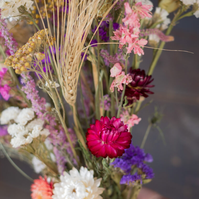 The Dried Flower Bouquet - Bright showcases a vibrant mix of pink, red, white, and purple flowers with wheat stalks, arranged against a blurred background.