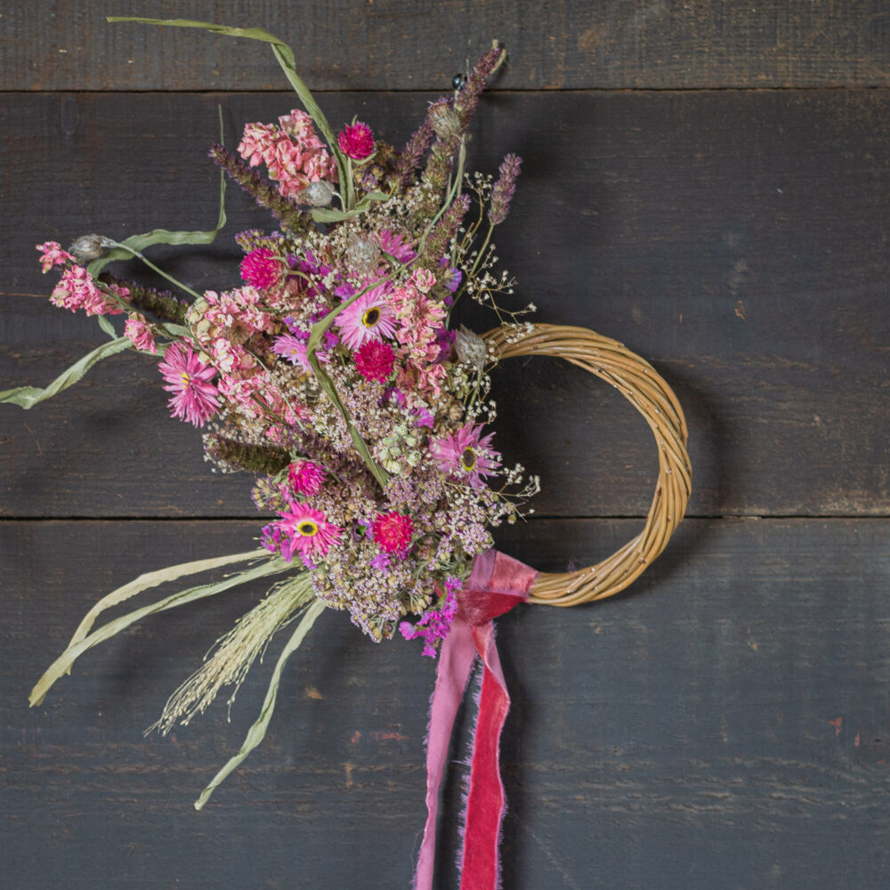 A small wreath adorned with rustic green and white dried flowers and grasses on a wooden background.