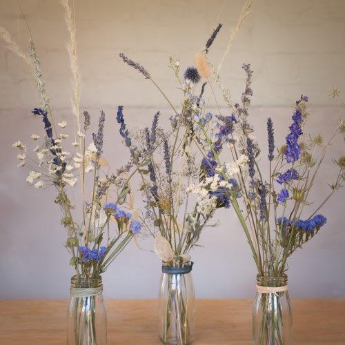 Three Letterbox Flowers glass jars beautifully display dried flowers in blue, white, and beige tones on a wooden surface.