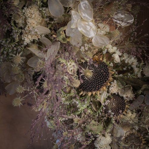 A close-up of the Everlasting "Light and Dark" Wreath displaying dried flowers with spiky black seed pods, delicate white blooms, transparent leaves, and wispy purple grasses.