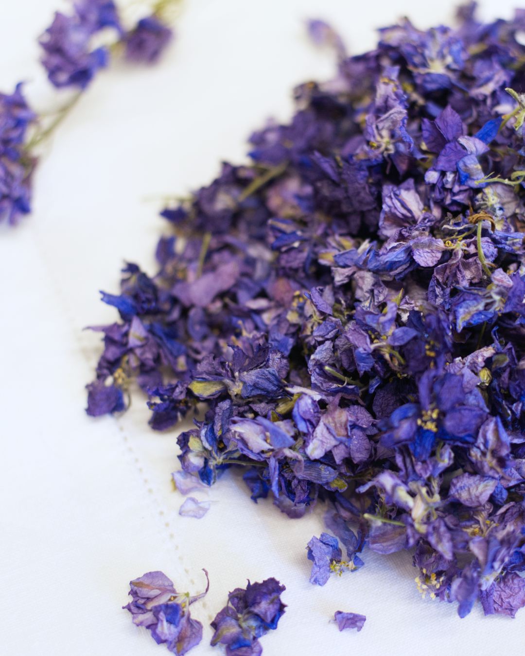 A close-up of dried blue larkspur confetti displayed on a white fabric surface.